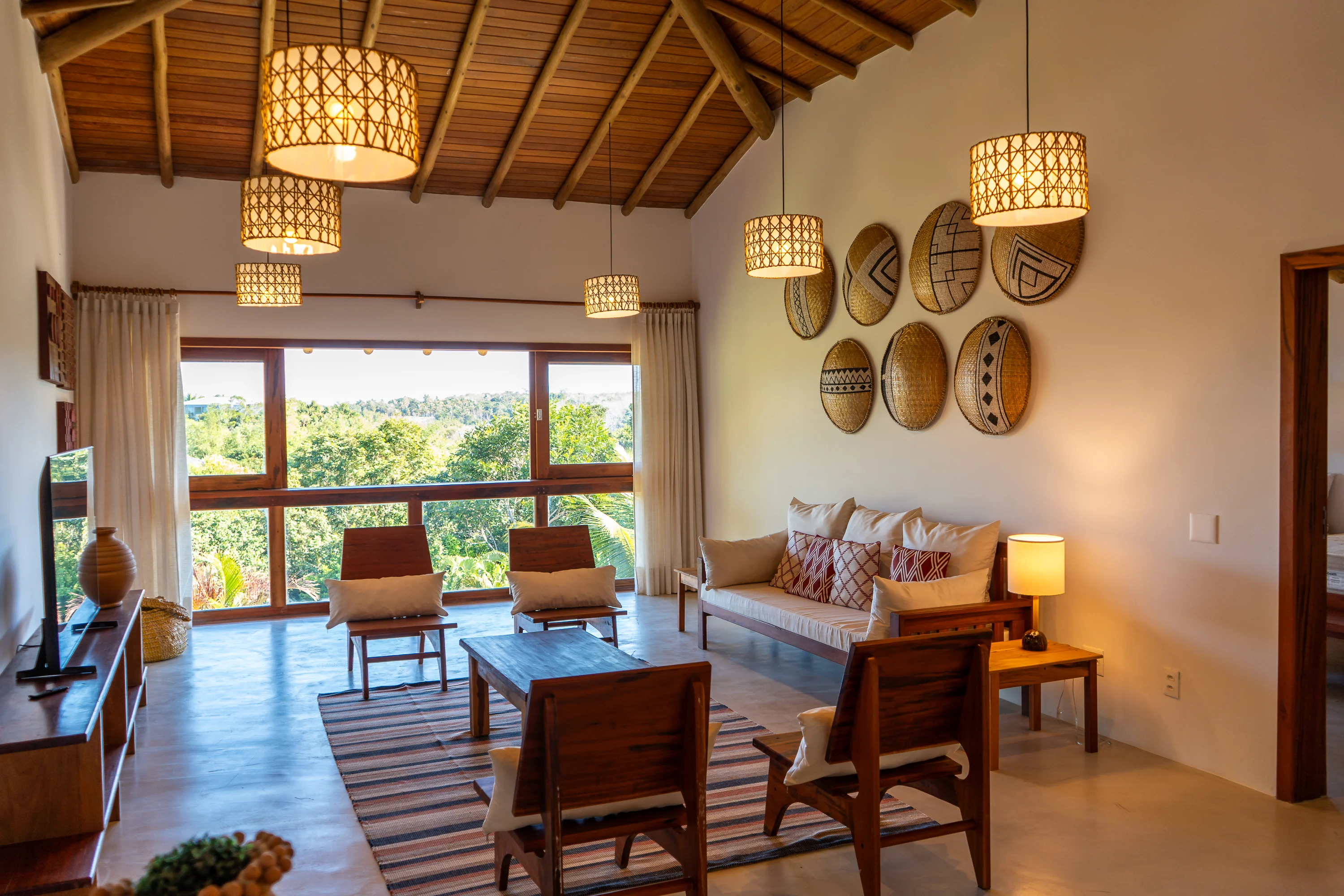Casa 21 - Wohnzimmer mit Sofa, Sesseln, Korbdekoration an der Wand und Fenstern mit Blick ins Grüne