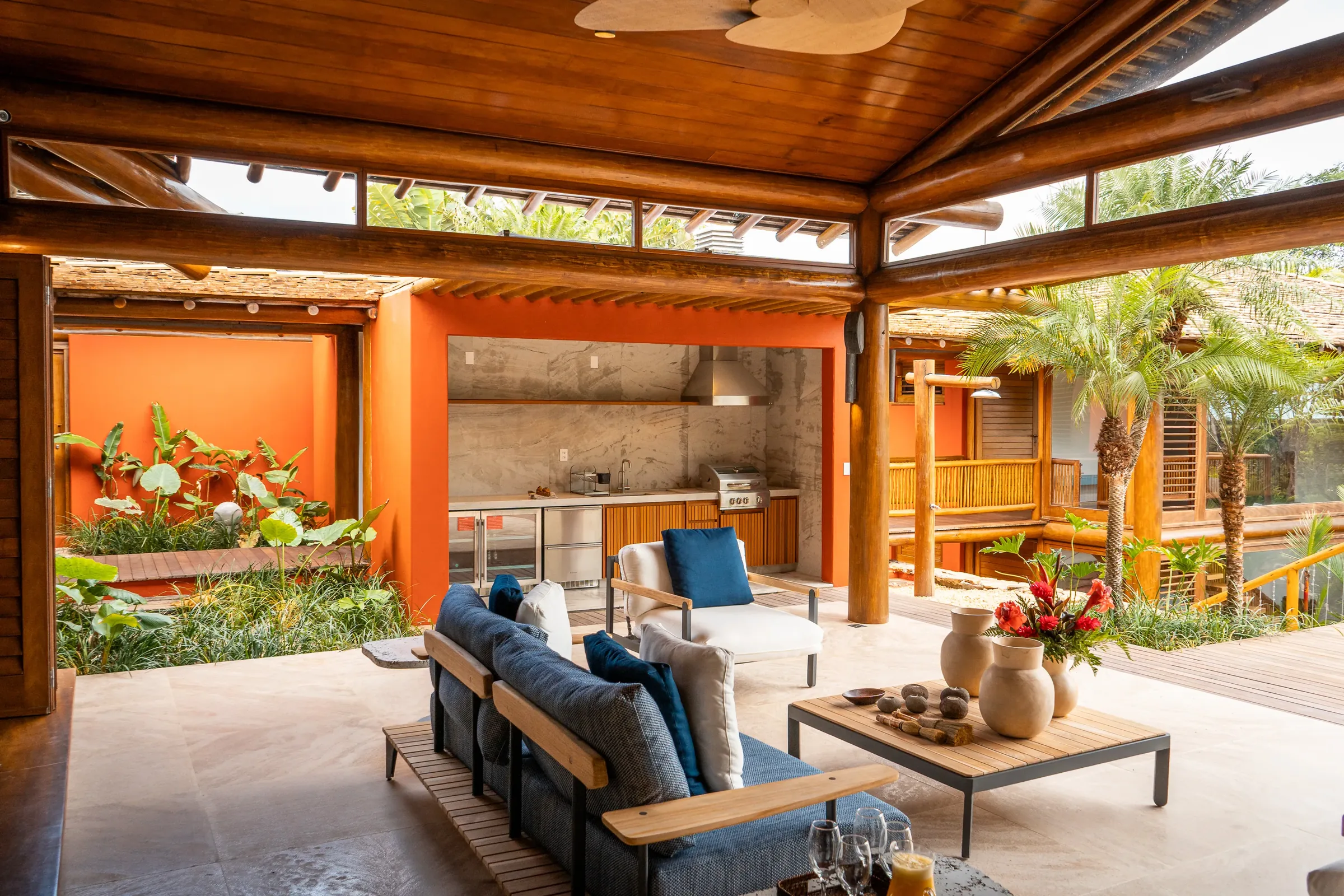 Casa 62 - estar externo com sofás azuis e a área gourmet ao fundo
