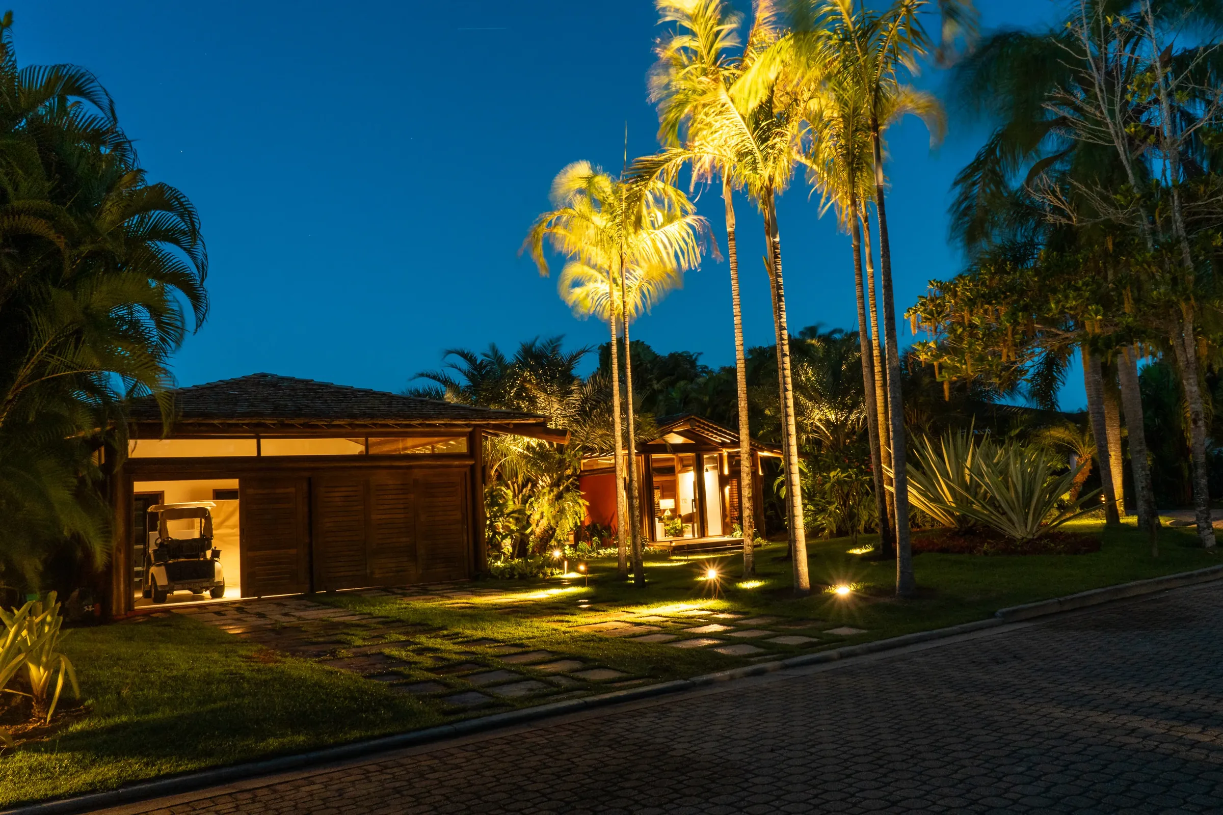Casa 62 - entrada iluminada à noite entre as palmeiras