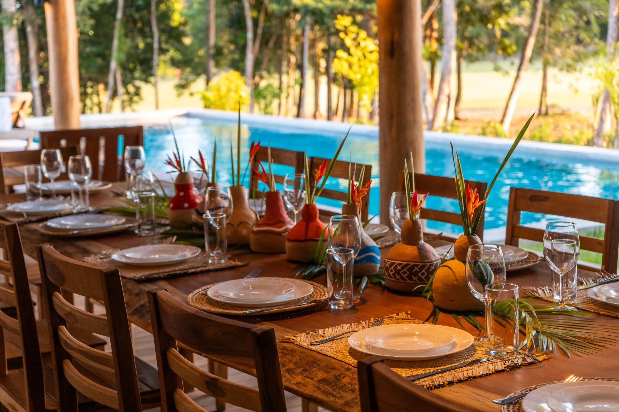 Mesa posta à beira da piscina, com louça de cerâmica e flores