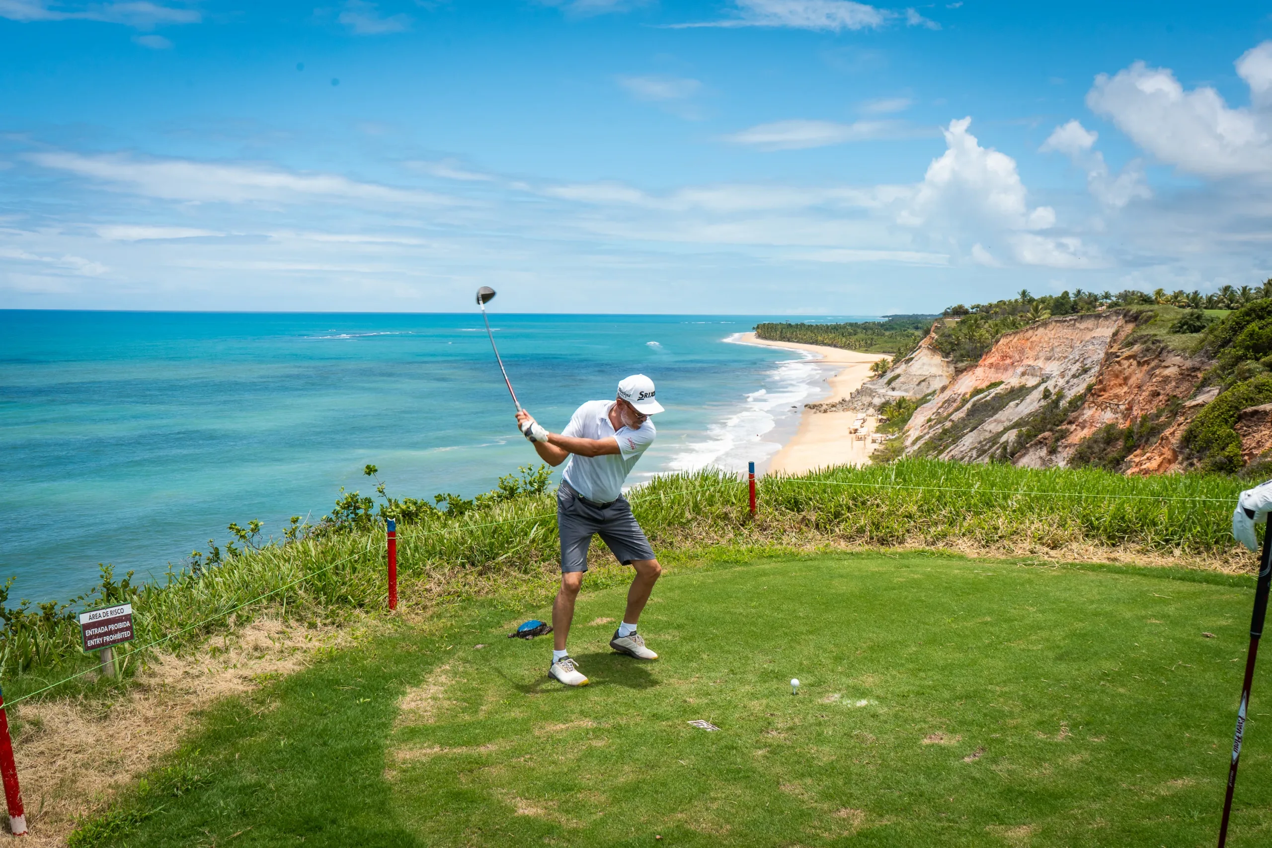 Golfista dando a tacada de saída sobre as falésias, com o mar ao fundo