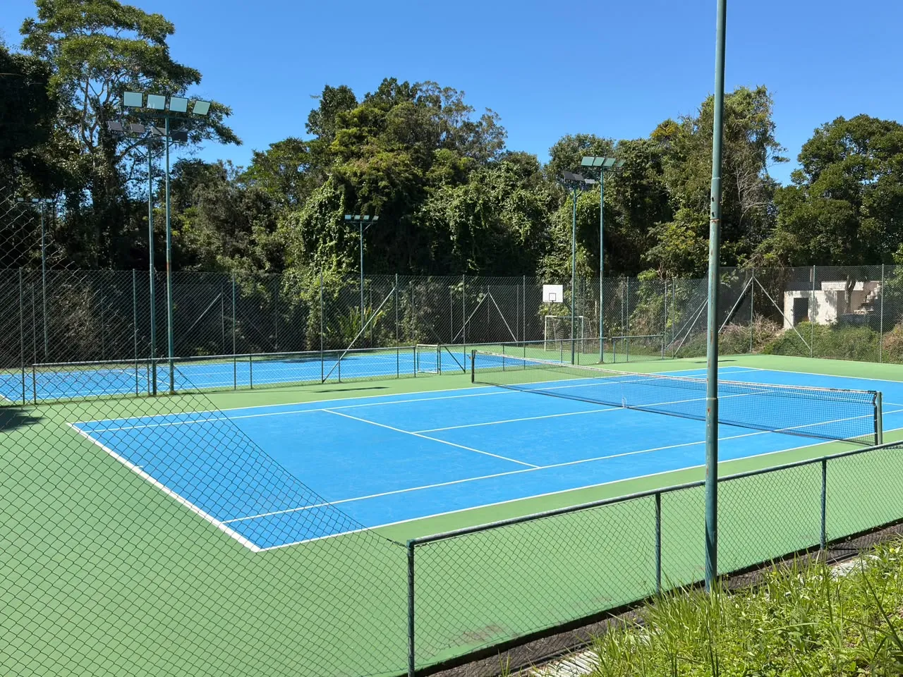 Cancha de tenis de Terravista, piso azul, con la cancha polideportiva al fondo y la mata atlántica alrededor.