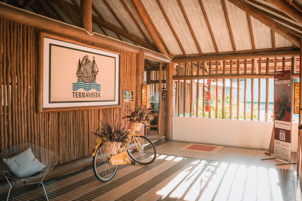 Recepção rústica com painel Terravista, bicicleta decorativa e piso em tons quentes.